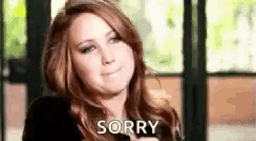 a woman is sitting in front of a window making a sorry face .