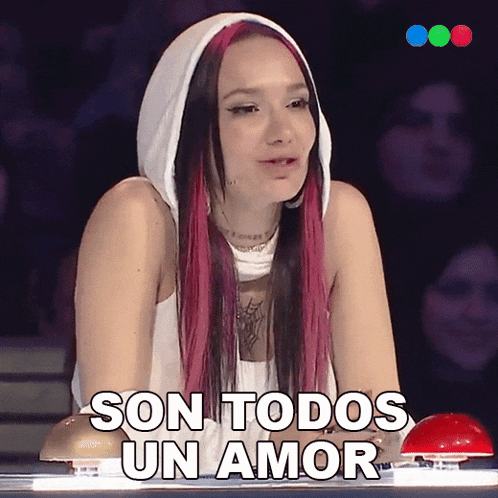 a woman with pink hair is sitting in front of a red button and says son todos un amor