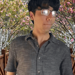 a man wearing glasses and a grey shirt is standing in front of a cherry blossom tree