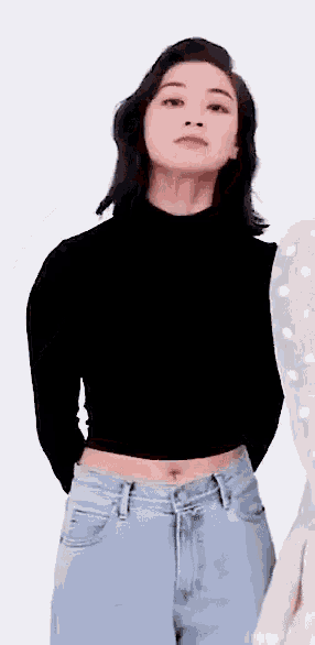 a woman in a black turtleneck and jeans is standing in front of a white background .