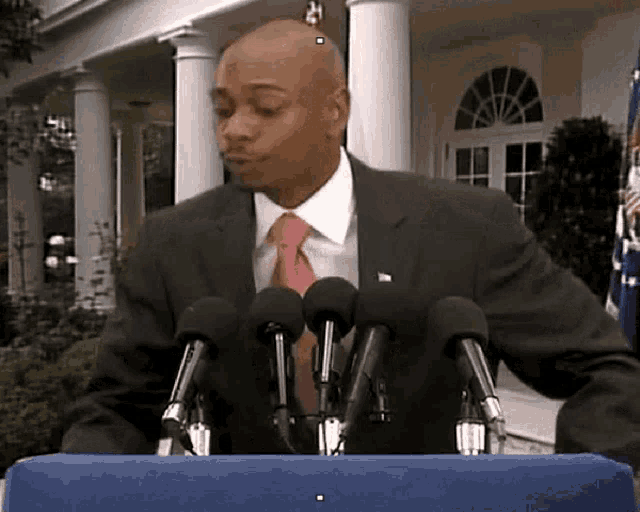 a man in a suit and tie is giving a speech in front of microphones