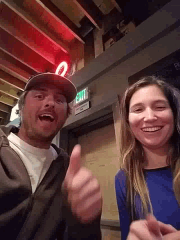 a man giving a thumbs up next to a woman in front of a sign that says exit