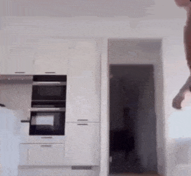 a person is jumping in the air in a kitchen with white cabinets and black appliances .