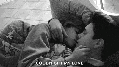 a black and white photo of a man and woman kissing while laying on a bed .