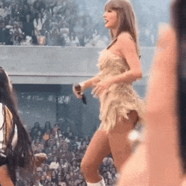a woman in a short dress is standing on a stage in front of a crowd holding a microphone .