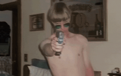 a man without a shirt is pointing a gun at the camera in front of a mirror that says ' brooklyn '