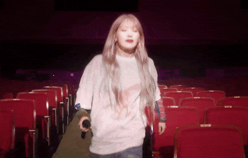 a woman in a white shirt is holding a microphone in an auditorium filled with red seats