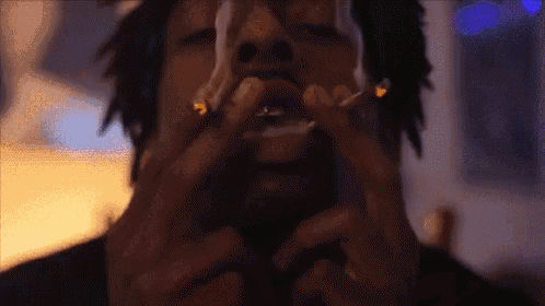 a man with dreadlocks is smoking a cigarette with smoke coming out of his mouth .