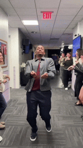 a man is dancing in a hallway with a red exit sign above him
