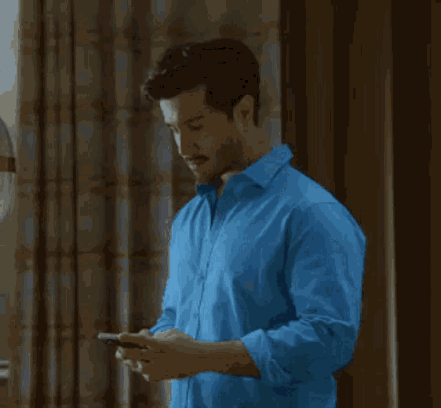 a man in a blue shirt is holding a cell phone in his right hand