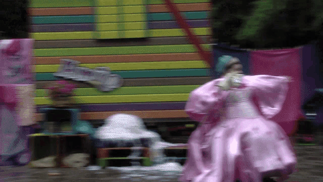 a woman in a pink dress is standing in front of a rainbow colored building