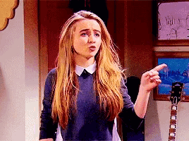 a girl with long blonde hair is pointing her finger at something .