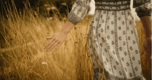 a woman in a dress holds a man 's hand in a field of tall grass