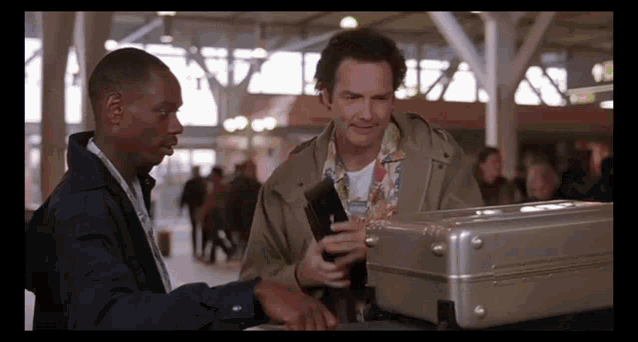 two men are standing next to a suitcase and one has a wallet in his hand