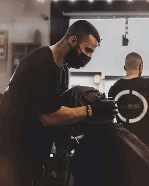 a man wearing a mask is cutting a man 's hair in a barber shop