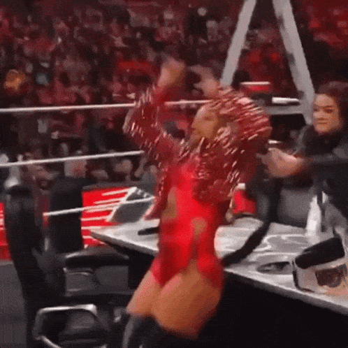 a woman in a red dress is standing in front of a table in a ring .