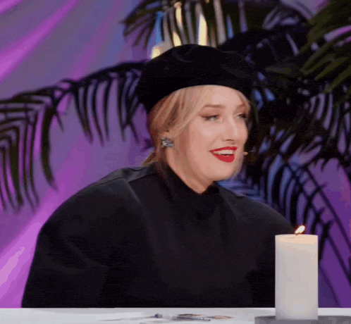 a woman wearing a black beret is sitting at a table next to a candle