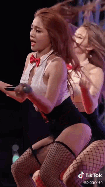 two women are dancing on a stage and one of them is wearing fishnet stockings and a bow tie .
