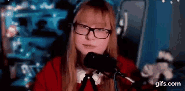 a girl wearing glasses is sitting in front of a microphone and talking into it .
