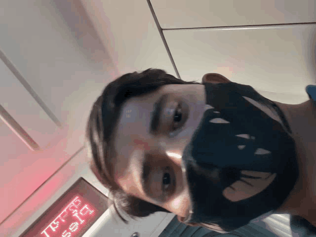 a man wearing a face mask is standing in front of a sign that says ' tesla ' on it