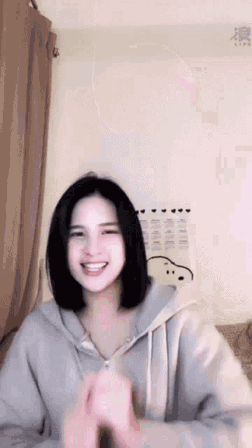 a young woman in a hoodie is smiling and making a heart shape with her hands .