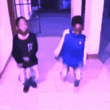 a blurry picture of two people walking down a hallway with one wearing a black shirt with the letter t on it