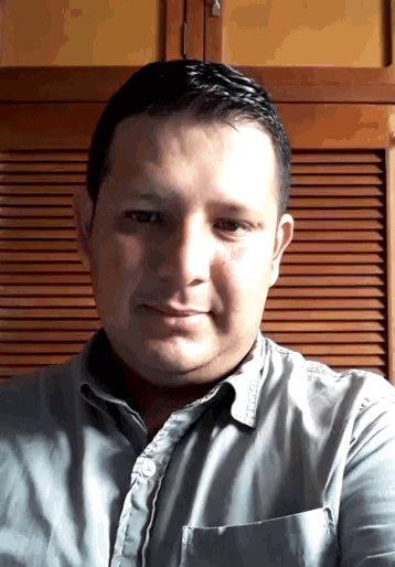 a man wearing a grey shirt is smiling in front of a wooden cabinet