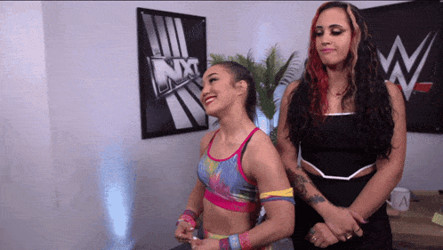 two female wrestlers stand in front of a sign that says nxt