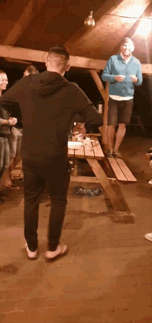 a man in a black hoodie stands in front of a wooden picnic table