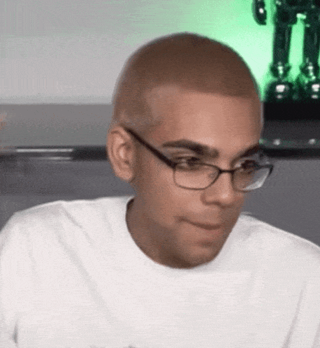 a young man wearing glasses and a white shirt is making a funny face .