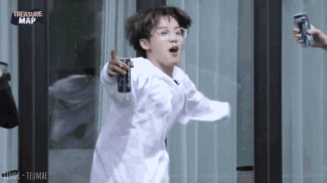 a young man in a white shirt is holding a can of soda while standing in front of a window .