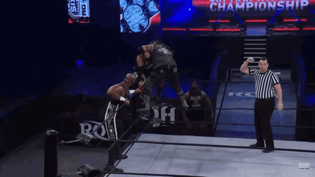 a referee watches two wrestlers in a ring with the word championship on the screen