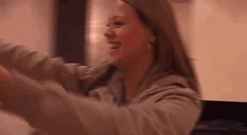 a woman is laughing with her arms outstretched while sitting on a couch .
