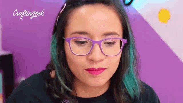 a woman wearing purple glasses and pink lipstick is looking down .