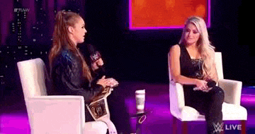 two women are sitting in chairs on a stage talking to each other in front of a microphone .