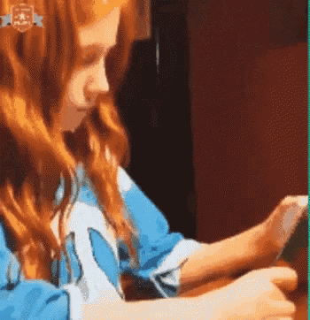 a girl with red hair is sitting at a table looking at her phone .