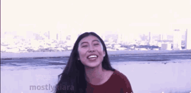 a woman in a red sweater is smiling in front of a city skyline and the word mostly is on the bottom