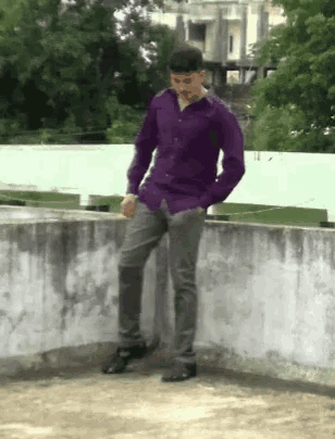a man in a purple shirt and gray pants is standing on a ledge