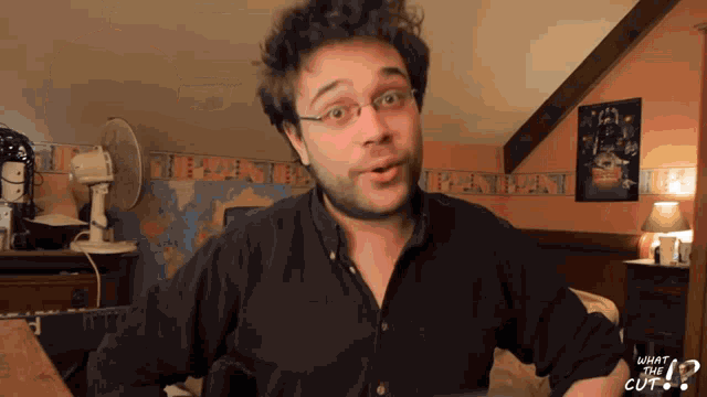 a man wearing glasses and a black shirt with what the cut written on the sleeve
