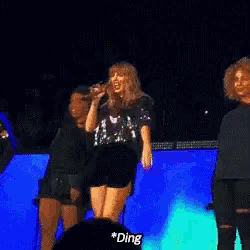 a woman is singing into a microphone while another woman stands behind her and says ding