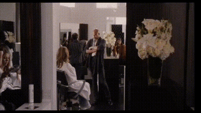 a woman is getting her hair done in a salon while a man stands in front of her
