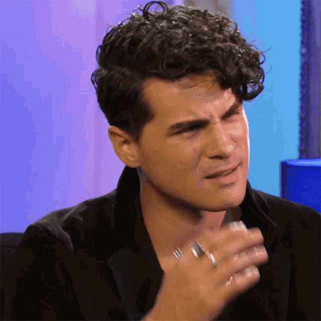 a man with curly hair and a ring on his finger is making a funny face