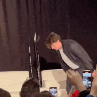 a man in a suit is standing on a stage in front of a crowd of people taking pictures of him .