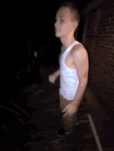 a young man in a white tank top and khaki shorts is standing on a wooden deck .