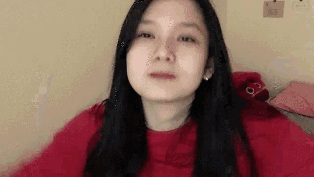 a woman in a red sweater is making a funny face while sitting on a bed .