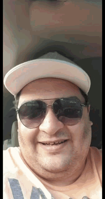 a man wearing sunglasses and a baseball cap smiles for the camera