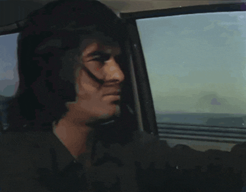 a man with long hair is sitting in a car and looking out the window