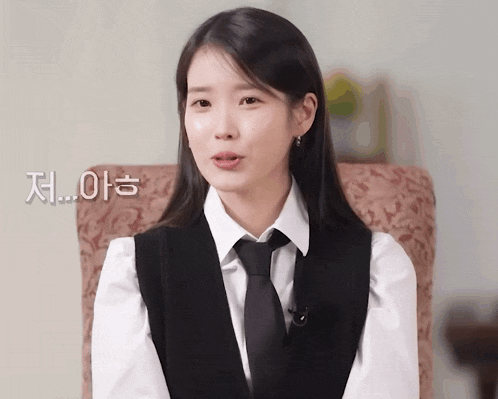 a woman in a white shirt and black tie is sitting in a chair with korean writing behind her