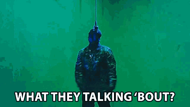 a man in a mask is standing in front of a green wall with the words what they talking bout .