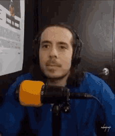 a man wearing headphones and a blue shirt is sitting in front of a yellow microphone .